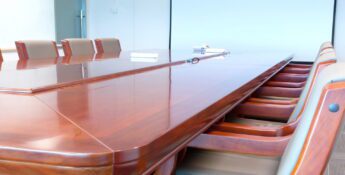 A long, polished wooden conference table with empty chairs is arranged in a meeting room, ready to strengthen your board of directors with strategic meetings against the backdrop of a blank screen.