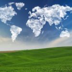 Clouds shaped like continents float in a blue sky above a green hilly landscape.