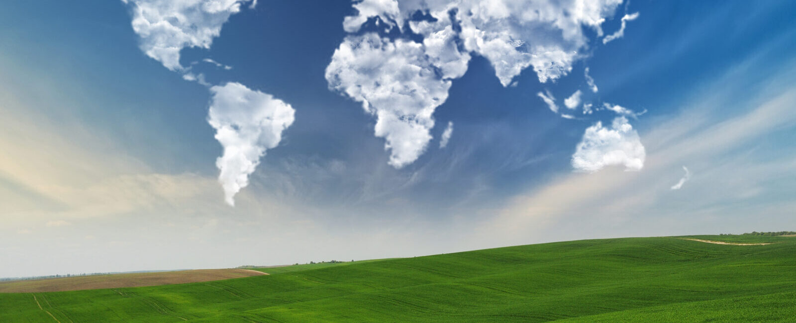 Clouds shaped like continents float in a blue sky above a green hilly landscape.