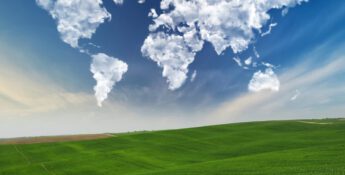 Clouds shaped like continents float in a blue sky above a green hilly landscape.
