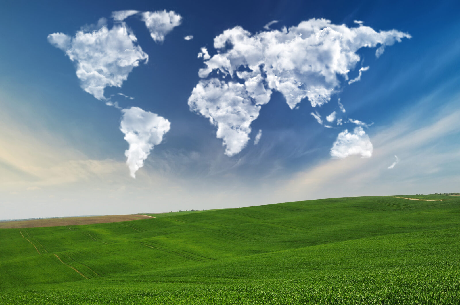 Clouds shaped like continents float in a blue sky above a green hilly landscape.