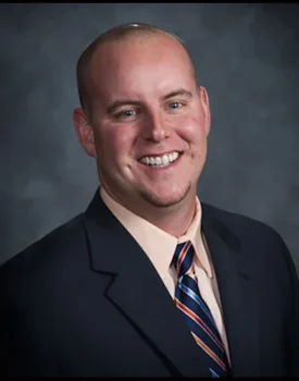A smiling man in a suit and tie, embodying the essence of Transactional Advisory, poses confidently against a dark gray background.