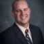 A smiling man in a suit and tie, embodying the essence of Transactional Advisory, poses confidently against a dark gray background.