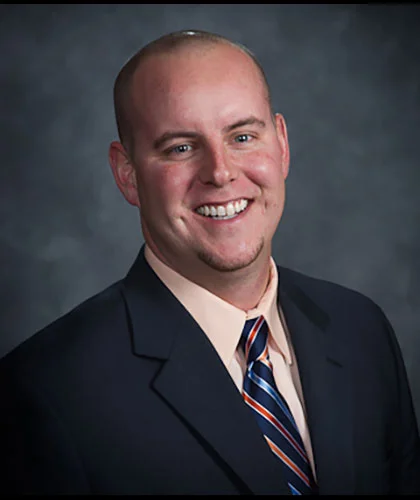 A smiling man in a suit and tie, embodying the essence of Transactional Advisory, poses confidently against a dark gray background.