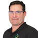 Man with short dark hair and glasses wearing a black collared shirt with a small colorful logo, standing against a plain white background.
