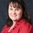 Roxie with shoulder-length dark hair wearing a red blouse, smiling confidently against a dark background, embodying the professionalism and expertise of transactional advisory.