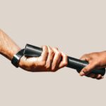 Two hands passing a black baton to each other, symbolizing a relay race or transfer of responsibility, against a plain background.
