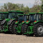 Four green tractors are parked in a row on a gravel lot with trees in the background, illustrating the kind of inventory affected by recent tax changes for equipment dealers.
