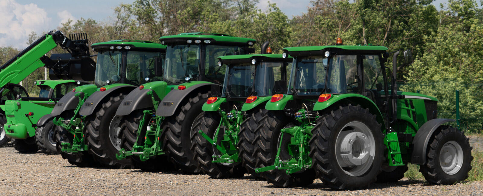 Four green tractors are parked in a row on a gravel lot with trees in the background, illustrating the kind of inventory affected by recent tax changes for equipment dealers.