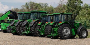 Four green tractors are parked in a row on a gravel lot with trees in the background, illustrating the kind of inventory affected by recent tax changes for equipment dealers.