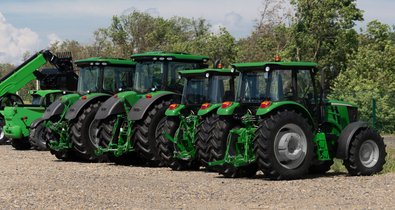 Four green tractors are parked in a row on a gravel lot with trees in the background, illustrating the kind of inventory affected by recent tax changes for equipment dealers.
