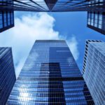 View from ground level looking up at several tall glass skyscrapers, reflecting the sky—much like pondering, What Happens to Your Bank-Owned Life Insurance?—all set against a backdrop of blue sky with drifting clouds.