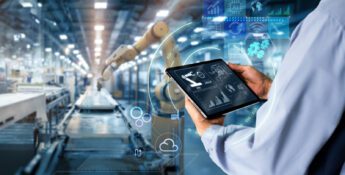 A person holds a tablet displaying data analytics and automation icons, overseeing robotic arms in a modern manufacturing facility—showcasing an essential AI business strategy for manufacturers in 2025.
