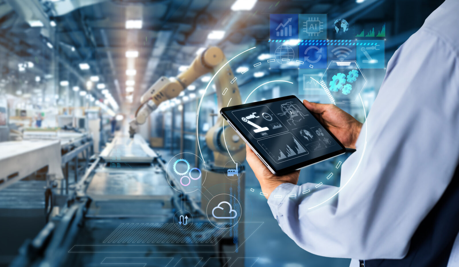 A person holds a tablet displaying data analytics and automation icons, overseeing robotic arms in a modern manufacturing facility—showcasing an essential AI business strategy for manufacturers in 2025.