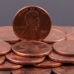 A group of U.S. one cent coins, with one 1997 penny standing upright among others lying flat on a dark background.