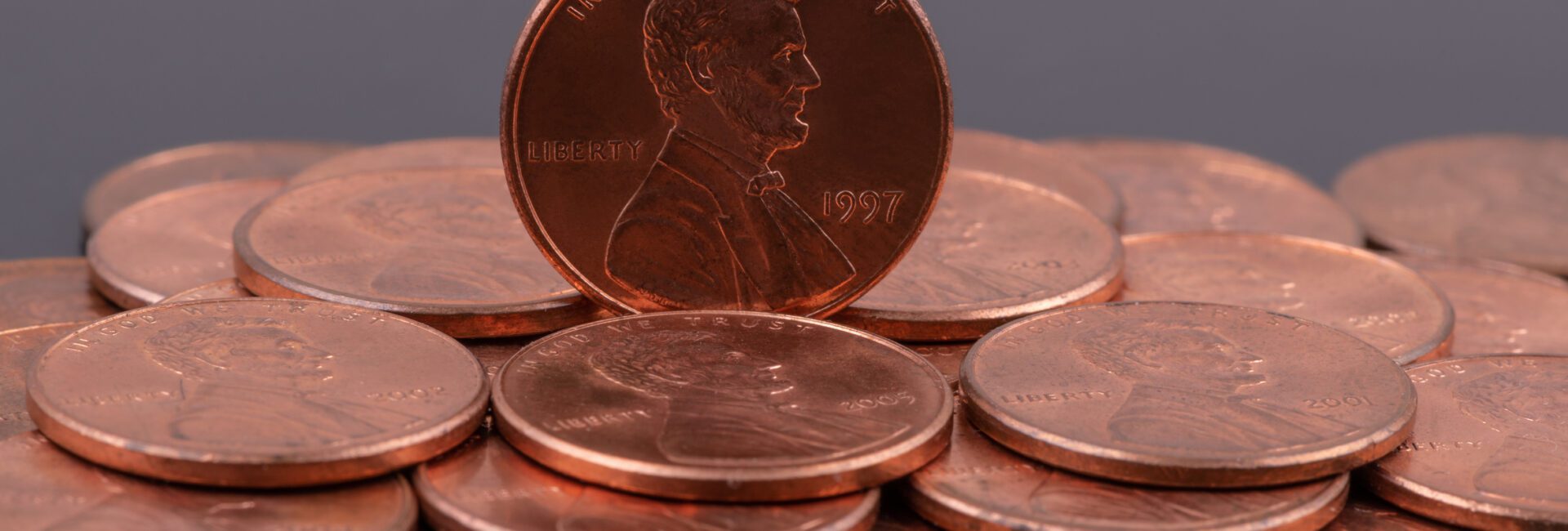 A group of U.S. one cent coins, with one 1997 penny standing upright among others lying flat on a dark background.