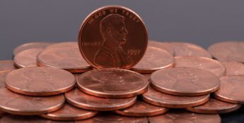 A group of U.S. one cent coins, with one 1997 penny standing upright among others lying flat on a dark background.