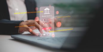A person uses a laptop with a floating mobile banking login screen and multiple warning symbols, highlighting the importance of strengthening mobile banking defenses against cyber security threats.