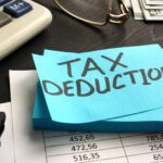 A sticky note with "TAX DEDUCTION" written on it sits on financial documents, highlighting Charitable Donations With Key Tax Strategies, next to a calculator, marker, eyeglasses, and cash.