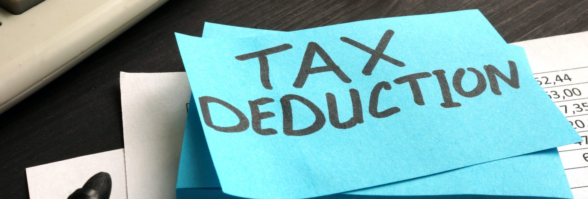 A sticky note with "TAX DEDUCTION" written on it sits on financial documents, highlighting Charitable Donations With Key Tax Strategies, next to a calculator, marker, eyeglasses, and cash.