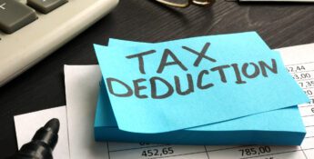 A sticky note with "TAX DEDUCTION" written on it sits on financial documents, highlighting Charitable Donations With Key Tax Strategies, next to a calculator, marker, eyeglasses, and cash.