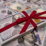 A stack of hundred dollar bills tied with a red ribbon rests on a surface scattered with more bills, symbolizing charitable donations with key tax strategies in mind.