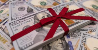A stack of hundred dollar bills tied with a red ribbon rests on a surface scattered with more bills, symbolizing charitable donations with key tax strategies in mind.