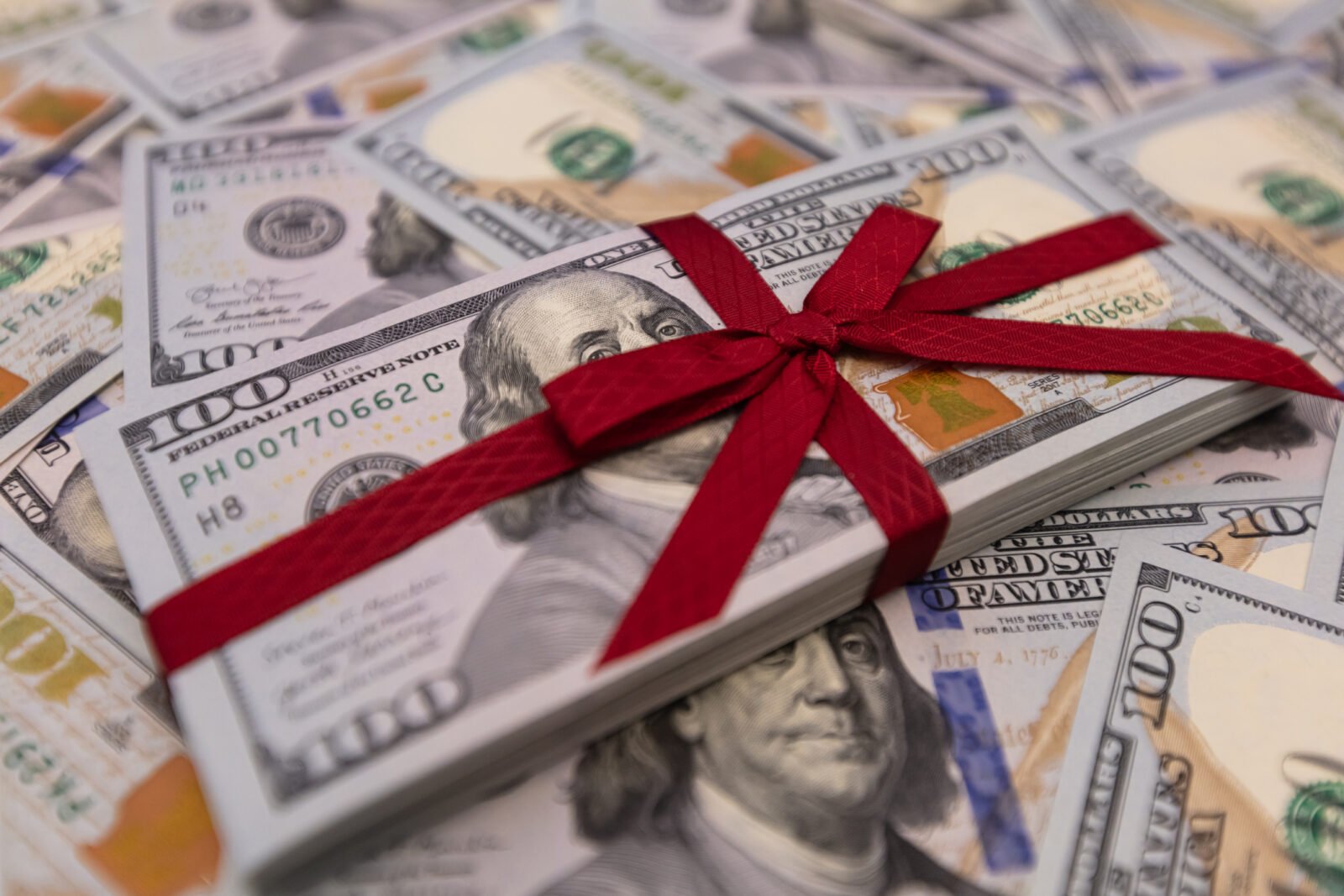 A stack of hundred dollar bills tied with a red ribbon rests on a surface scattered with more bills, symbolizing charitable donations with key tax strategies in mind.