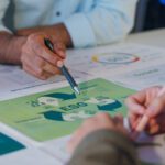 Three people discuss documents on a table, focusing on a green ESG (Environmental, Social, Governance) chart and exploring sustainability strategies with materiality assessments among other printed materials.