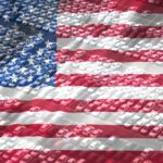Rows of cars in a parking lot overlaid with a transparent image of the United States flag, symbolizing Charitable Donations With Key Tax Strategies.