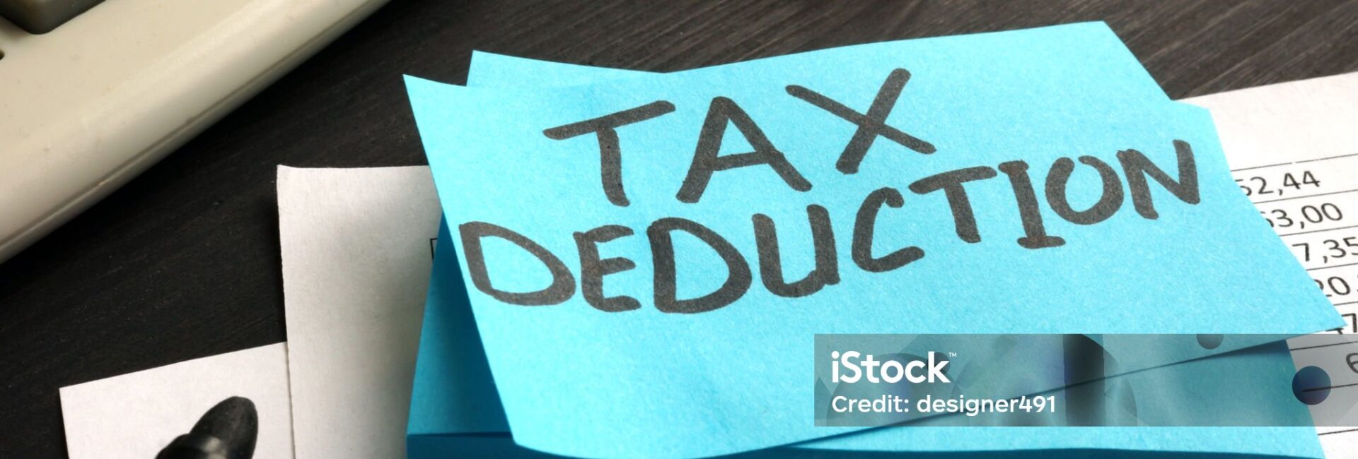 A blue sticky note with "TAX DEDUCTION" written on it sits on financial documents, near a calculator, pen, glasses, and cash—highlighting the impact of New IRS Updates to Section 139L Loan Interest.