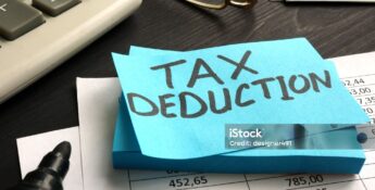 A blue sticky note with "TAX DEDUCTION" written on it sits on financial documents, near a calculator, pen, glasses, and cash—highlighting the impact of New IRS Updates to Section 139L Loan Interest.