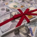 A stack of 100-dollar bills tied with a red ribbon rests atop scattered bills, symbolizing Charitable Donations With Key Tax Strategies.