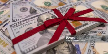 A stack of 100-dollar bills tied with a red ribbon rests atop scattered bills, symbolizing Charitable Donations With Key Tax Strategies.