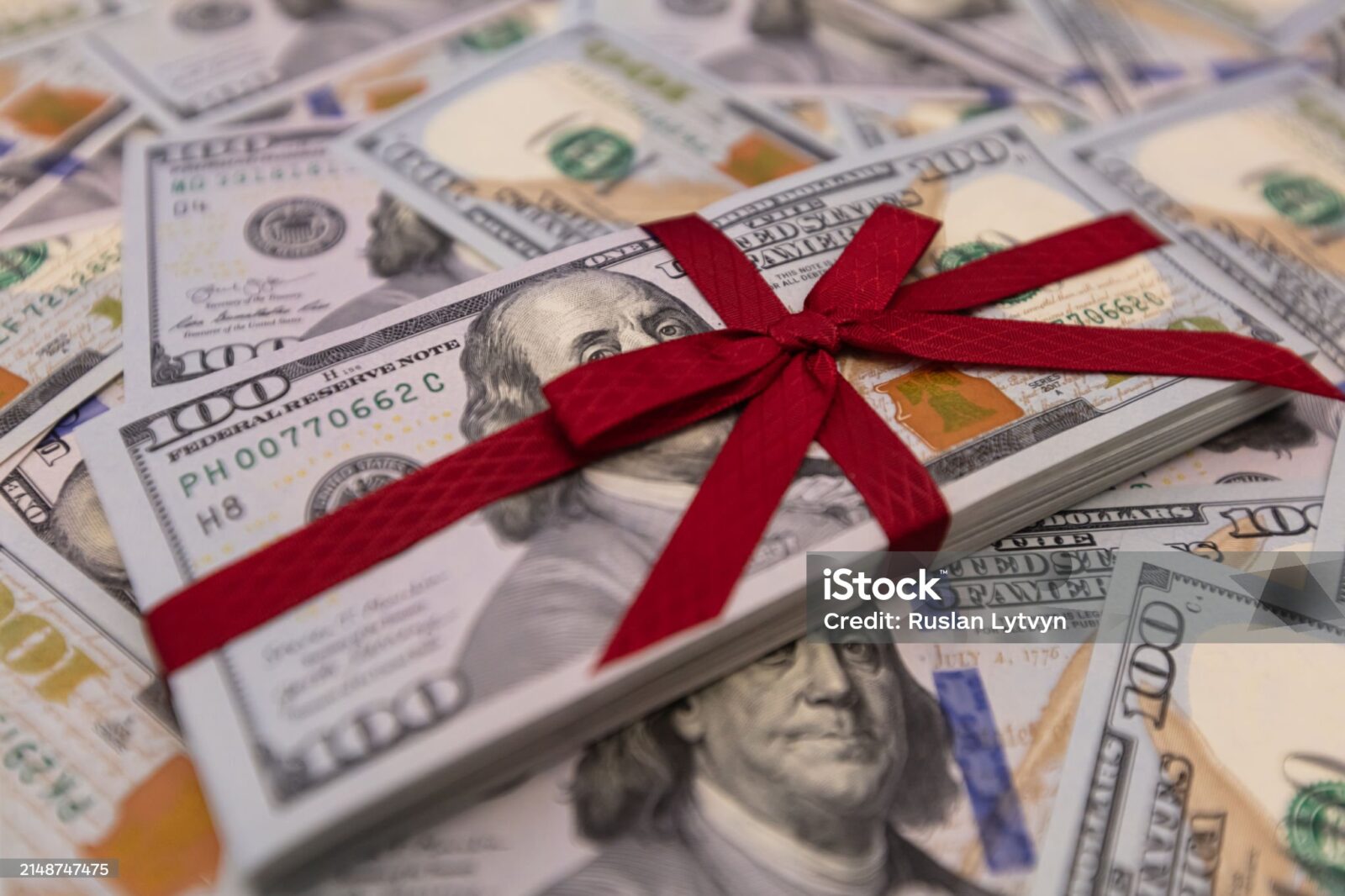 A stack of 100-dollar bills tied with a red ribbon rests atop scattered bills, symbolizing Charitable Donations With Key Tax Strategies.
