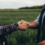 A man and woman from Sustainability Peer Groups shake hands in a field, fostering collaboration for a greener future.