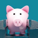 A pink piggy bank is held tightly in a metal vise against a blue background.