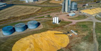 Aerial view of an agricultural facility with large grain silos, storage tanks, and piles of harvested grain spread on the ground, illustrating preparations for biofuels volatility in today's evolving energy landscape.