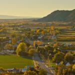 A small rural town with houses, roads, fields, and trees nestles in a valley beneath mountains and a clear sky, as news spreads that Pinion & TCA announce intent to merge.