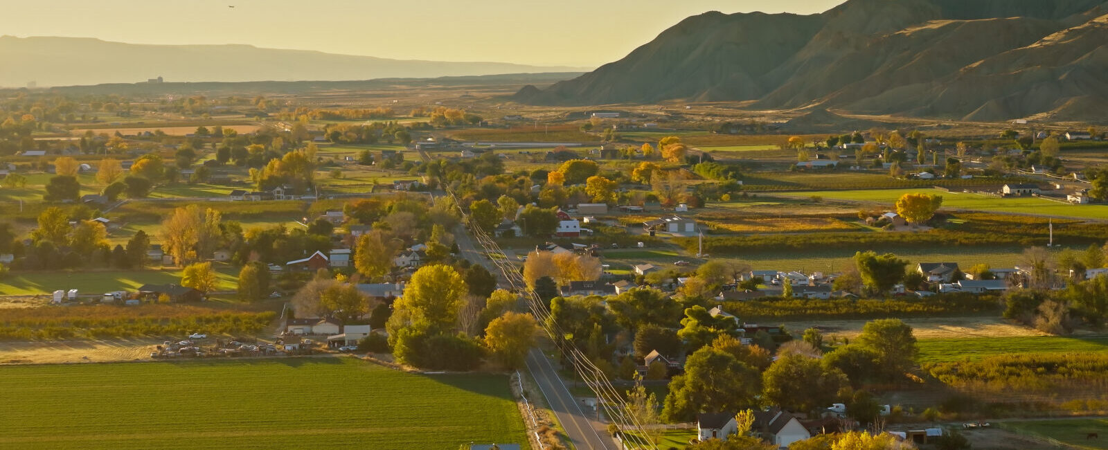 A small rural town with houses, roads, fields, and trees nestles in a valley beneath mountains and a clear sky, as news spreads that Pinion & TCA announce intent to merge.