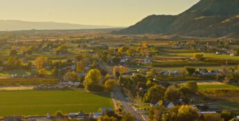 A small rural town with houses, roads, fields, and trees nestles in a valley beneath mountains and a clear sky, as news spreads that Pinion & TCA announce intent to merge.