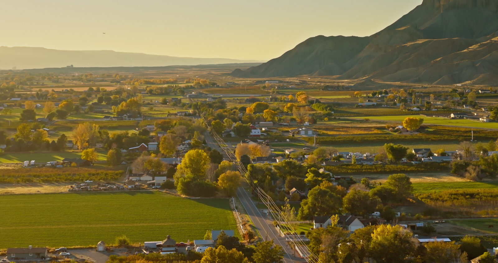 A small rural town with houses, roads, fields, and trees nestles in a valley beneath mountains and a clear sky, as news spreads that Pinion & TCA announce intent to merge.