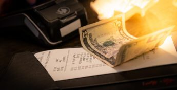 A restaurant bill with a twenty-dollar bill placed on top, next to a payment terminal on a dimly lit table.