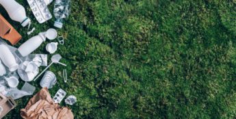 Assorted household waste, including plastic bottles, cans, paper, and blister packs—often subject to Extended Producer Responsibility (EPR)—lies on the left side of a green grass surface, with empty space on the right.