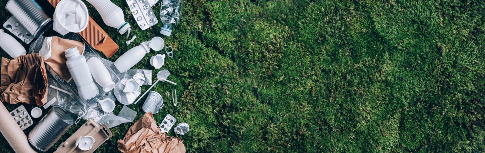 Assorted household waste, including plastic bottles, cans, paper, and blister packs—often subject to Extended Producer Responsibility (EPR)—lies on the left side of a green grass surface, with empty space on the right.