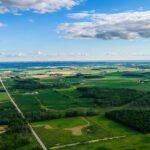 Aerial view of a rural landscape with green fields, scattered trees, and farmland, reflecting sustainable practices aligned with the Science Based Targets initiative (SBTi), under a partly cloudy blue sky.