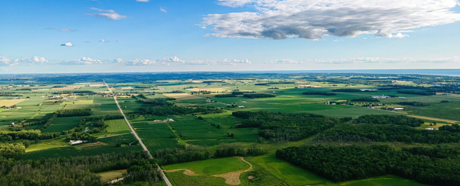 Aerial view of a rural landscape with green fields, scattered trees, and farmland, reflecting sustainable practices aligned with the Science Based Targets initiative (SBTi), under a partly cloudy blue sky.