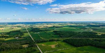 Aerial view of a rural landscape with green fields, scattered trees, and farmland, reflecting sustainable practices aligned with the Science Based Targets initiative (SBTi), under a partly cloudy blue sky.
