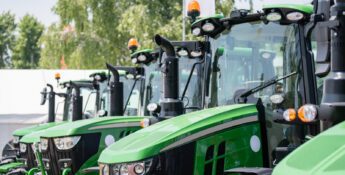 A row of new green tractors with large tires and orange lights is parked outdoors on a sunny day.