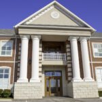 Two-story red brick building with large white columns, a peaked roof, and symmetrical windows, symbolizing stability—just as understanding what the Revised CBLR Rule means for growing community banks ensures a strong foundation on a clear day.